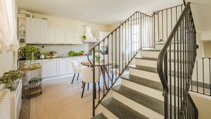 A modern kitchen with white cabinets, a dining area with a round table, and a spiral staircase with black railings. - Comfortable Convenient Apartment with Garden Views (Lucca)
