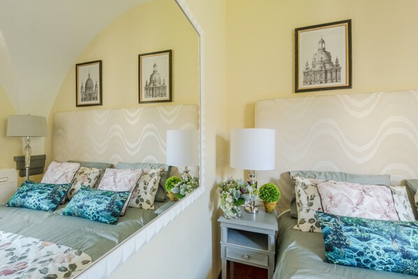 A hotel room with two beds, each with floral-patterned bedding and pillows, a nightstand with a lamp, and framed pictures on the wall. - Comfortable Convenient Apartment with Garden Views (Lucca)
