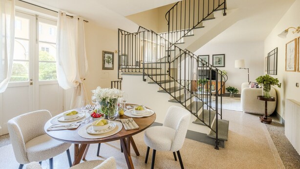 A dining area with a round table set for four, a staircase with a metal railing, and a living area with a sofa and a lamp. - Comfortable Convenient Apartment with Garden Views (Lucca)
