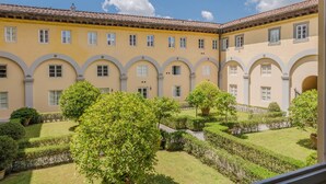 A courtyard with a yellow building featuring arched windows and a tiled roof. - Comfortable Convenient Apartment with Garden Views (Lucca)