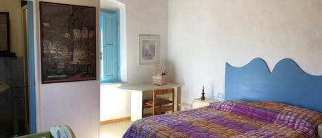 A bedroom with a colorful bedspread, a blue headboard, a desk with a chair, and a framed picture on the wall.