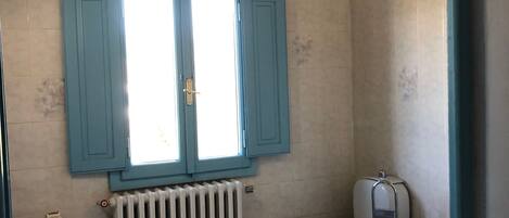 A bathroom with a white sink, toilet, and bathtub, a window with blue shutters, and a radiator.