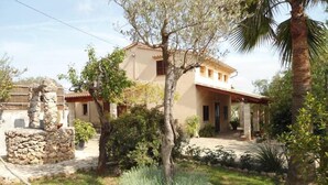 A two-story house with a stone structure in the front, surrounded by greenery and a palm tree. - House / Villa - Selva (Caimari)