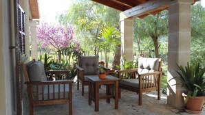 An outdoor patio with wooden furniture, including chairs and a table, surrounded by potted plants and trees. - House / Villa - Selva (Caimari)