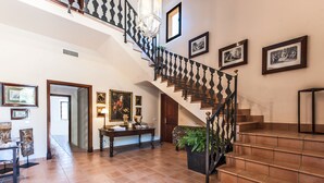 A spacious foyer with a grand staircase, a dining area, and a hallway leading to a bedroom.