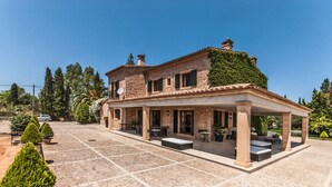A two-story house with a covered patio area, stone walls, and a garden with potted plants.