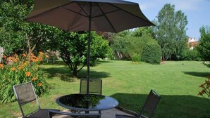 An outdoor patio with a round table and two chairs, a large umbrella, and a well-maintained lawn. - COMFORT air-conditioned house with garden, terrace in Medieval City in Burgundy (Semur-En-Auxois)