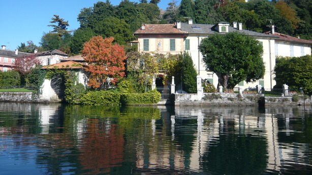 Una vista tranquila sobre el lago, con un edificio blanco de techo con tejas y un jardín delantero.