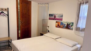 Een slaapkamer met een bed, een houten deur, een klein tafeltje en twee aan de muur bevestigde schilderijen.