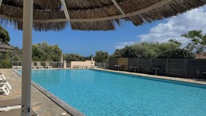 Una piscina con sillones de descanso y sombrillas, rodeada por una terraza de piedra y una valla de madera.