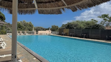 Une piscine entourée d’un sol en pierre et d’une clôture en bois, avec des chaises longues et des parasols à proximité.