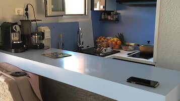 Une cuisine moderne avec un plan de travail blanc, une machine à café, une bouilloire et un téléphone intelligent posés sur le plan de travail.