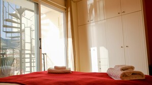 Une chambre d ’hôtel avec un lit, une couverture rouge et un ensemble de serviettes. Il y a une fenêtre donnant sur un immeuble et une chaise à l’extérieur.