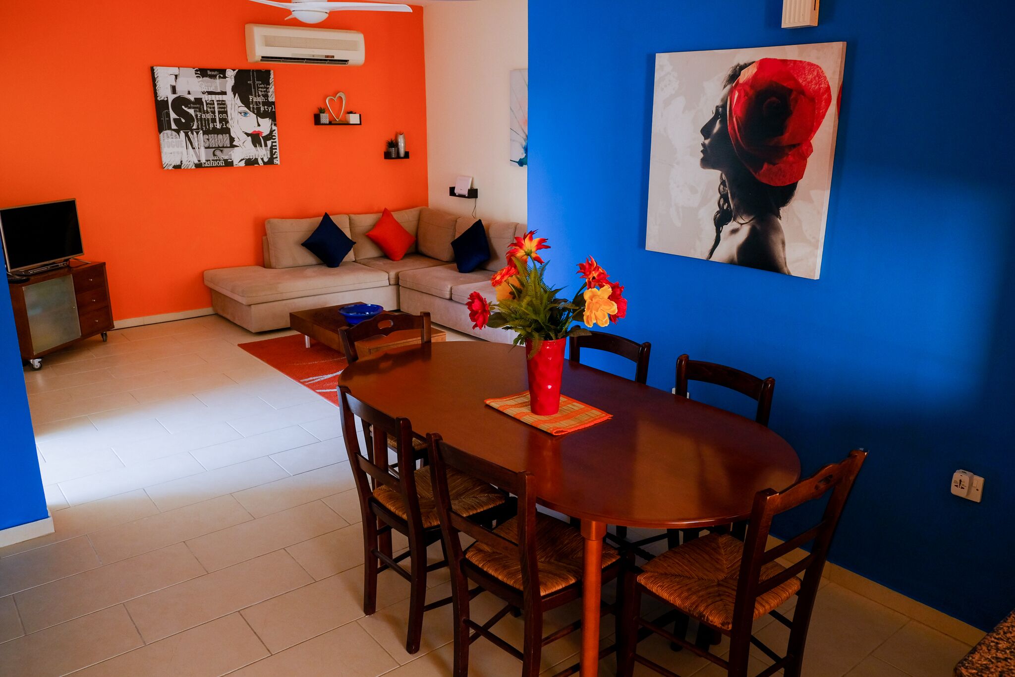 Un comedor con una mesa y sillas de madera, un florero con flores y una pared azul con un cuadro.