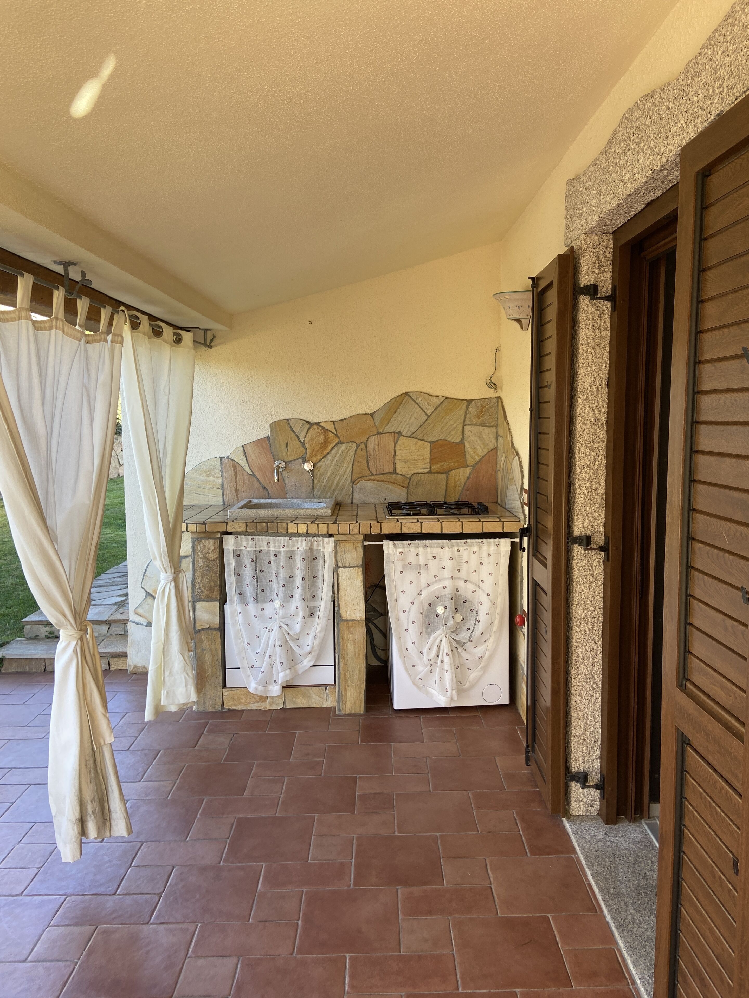 An outdoor kitchen area with stone backsplash, a gas stove, and a tiled floor.