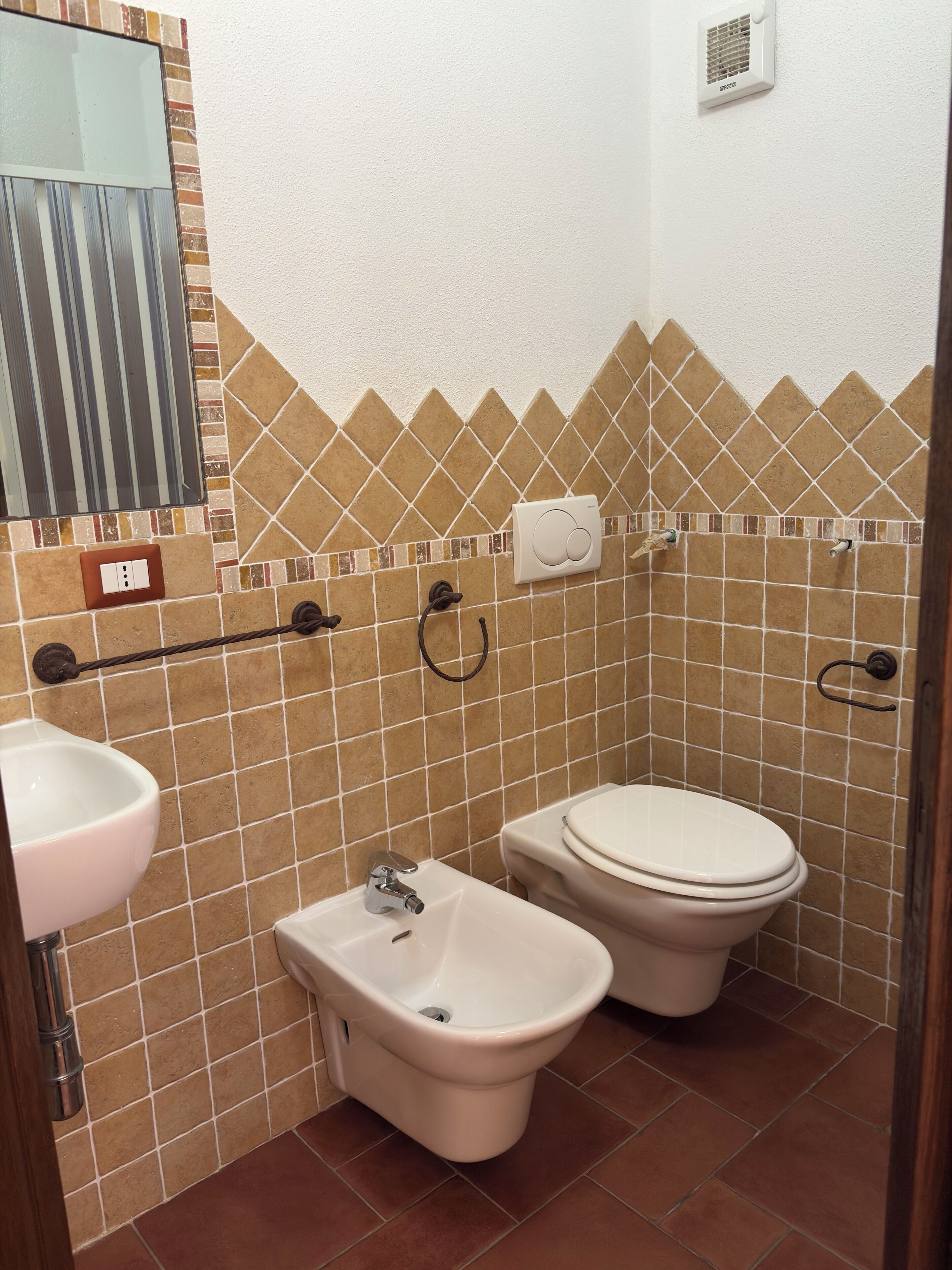 Een badkamer met twee toiletten, een toiletbrons, een wastafel en een spiegel.
