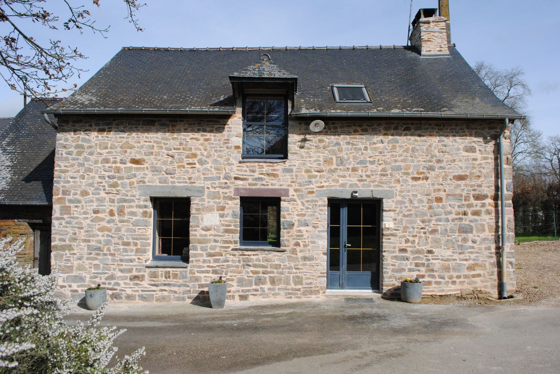 A stone building with a dark roof, two windows, a door, and a chimney.