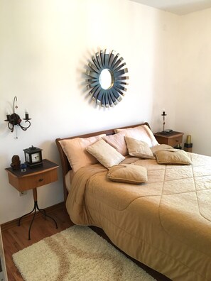 Une chambre à coucher comprenant un lit, une table de chevet, une commode, un miroir fixé au mur et une applique murale.