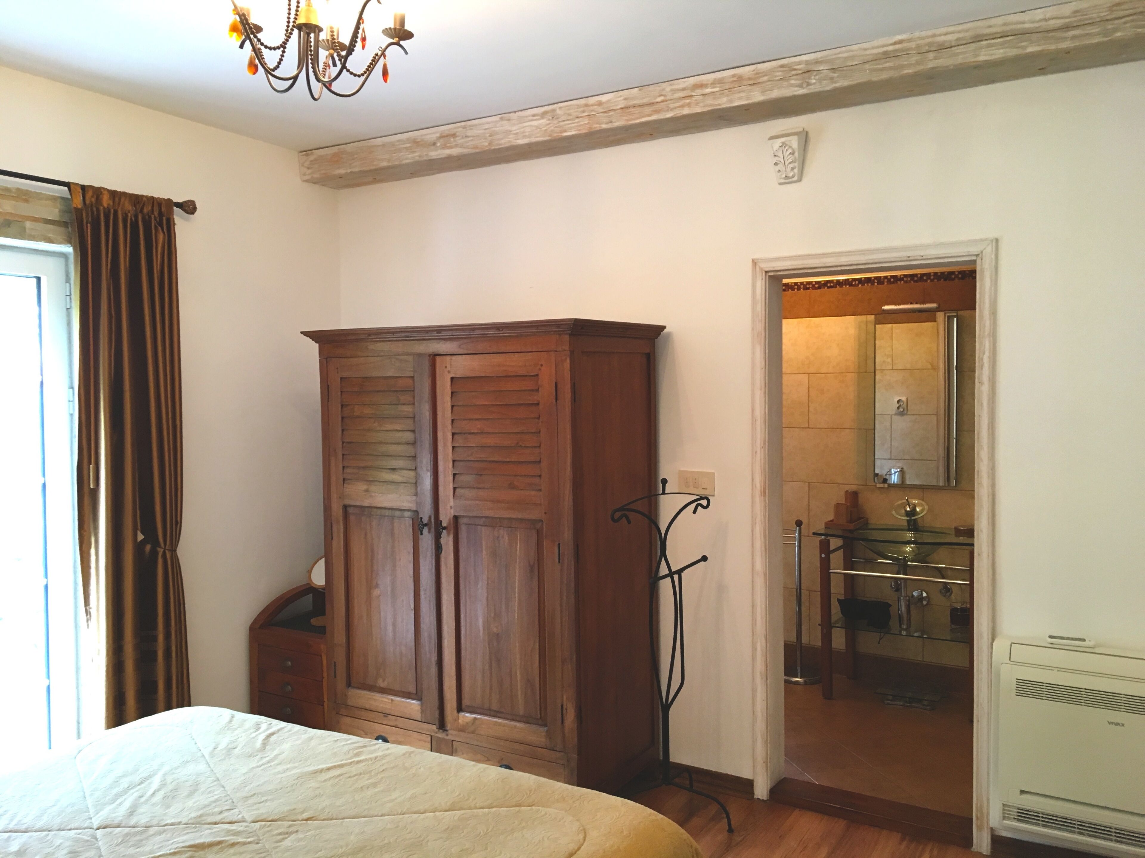 A bedroom with a large wardrobe, a bed, a chandelier, and a bathroom visible through an open door.