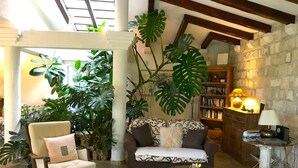 A cozy living room with a sofa, armchair, and coffee table, surrounded by large plants and a bookshelf. - Large Luxury Stone Villa With Private Infinity Pool And Sea Views (Southern Coastal)