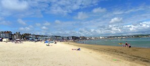 Une plage où des gens se prélassent au soleil et se baignent, avec des bâtiments en arrière-plan et un ciel dégagé.