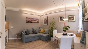 A modern living room with a grey sectional sofa, a white dining table, and a potted plant.