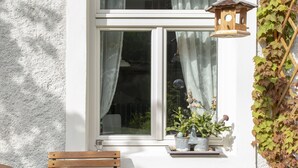 Een houten bank voor een raam, met een witte muur, een bloempot en een vogelhuisje.