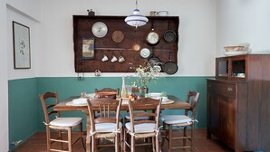 A dining area with a wooden table and chairs, a wall-mounted pan rack, and a cabinet with a glass door.