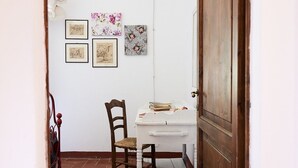 A narrow hallway with a wooden door, a white desk with a chair, and several framed artworks on the wall.