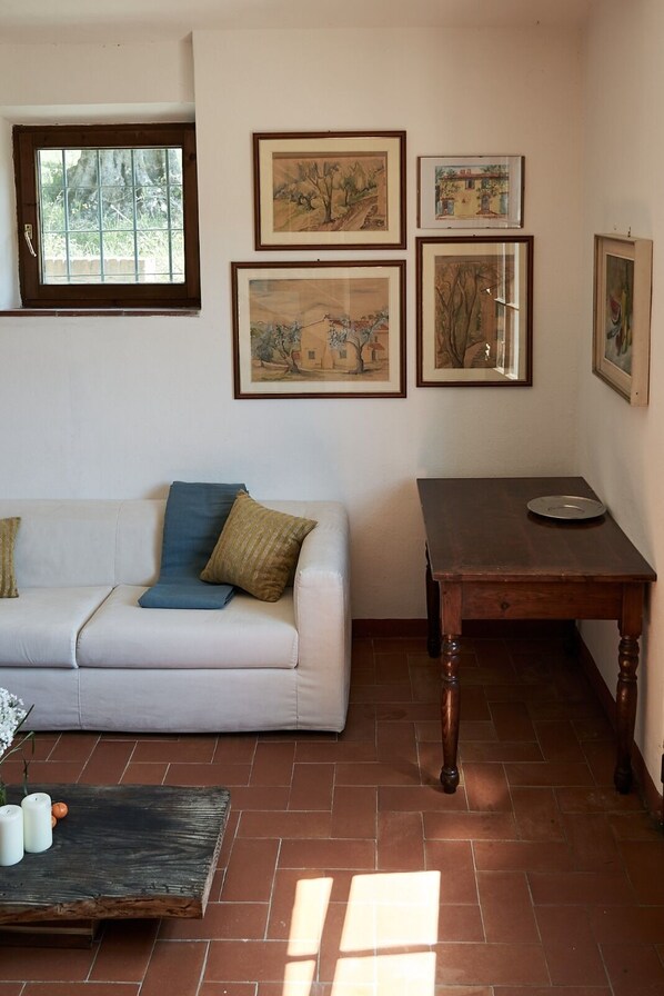 Uma sala de estar com um sofá branco, uma mesa de centro de madeira e uma mesinha lateral de madeira. Há quatro obras de arte emolduradas na parede.