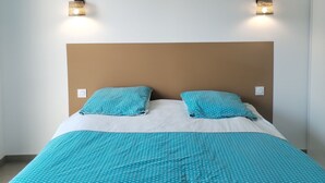 A bed with a blue patterned bedspread and pillows, two wall-mounted lights, and a hanging light fixture.