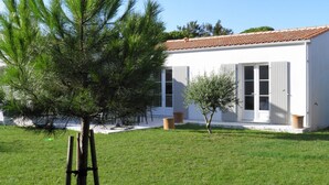 A white building with a tiled roof, a grassy yard, and two trees.