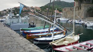 Um porto com diversos barcos atracados, um cais de pedra e edifícios ao fundo.