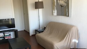 Uma sala de estar com sofá, televisão, luminária e estante de livros.