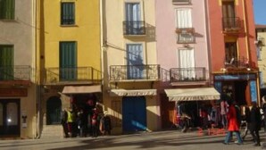 Uma fileira de edifícios coloridos com sacadas, uma rua em frente e pessoas caminhando.