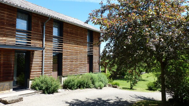 A modern building with horizontal wooden slats, large windows, and a gravel driveway. - Country Cottage / Gite - LA ROQUE GAGEAC (La Roque-Gageac)