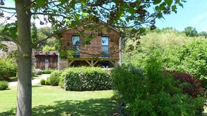 A rustic wooden house with a porch, surrounded by lush greenery and a well-maintained lawn. - Country Cottage / Gite - LA ROQUE GAGEAC (La Roque-Gageac)
