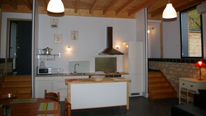 A modern kitchen with wooden beams, a central island, and a stone accent wall. - Country Cottage / Gite - LA ROQUE GAGEAC (La Roque-Gageac)
