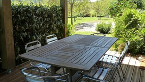 A covered patio with a wooden table and metal chairs, overlooking a landscaped garden. - Country Cottage / Gite - LA ROQUE GAGEAC (La Roque-Gageac)