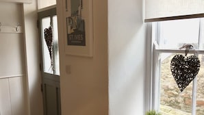 A kitchen with a white table, wooden chairs, a white cabinet, a window with a heart-shaped decoration, and a framed picture on the wall. - Fisherman's Cottage, fantastic Downalong location (Saint Ives)