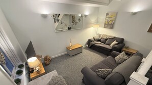 A modern living room with a grey sofa, a wooden side table, a lamp, and a mirror on the wall. - Fisherman's Cottage, fantastic Downalong location (Saint Ives)