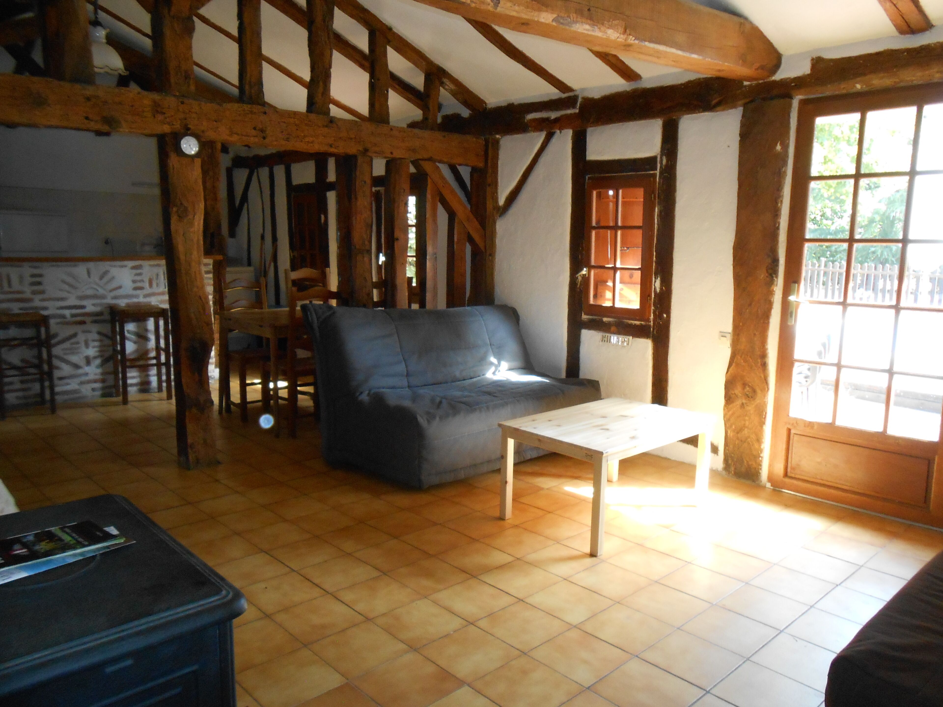 Une pièce rustique avec des poutres apparentes, un canapé gris, une petite table en bois et un sol carrelé.