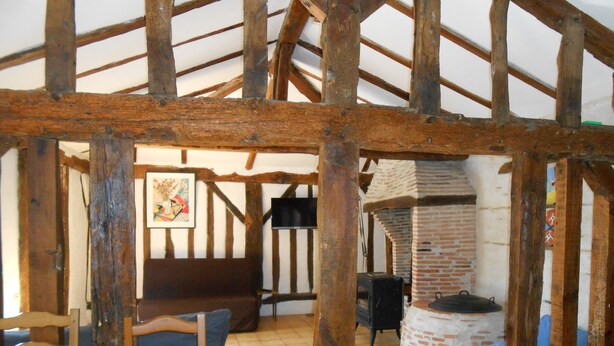 A rustic interior with exposed wooden beams, a brick oven, and a tiled floor.