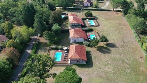 An aerial view of a residential area with two houses, each with a swimming pool and surrounded by greenery.