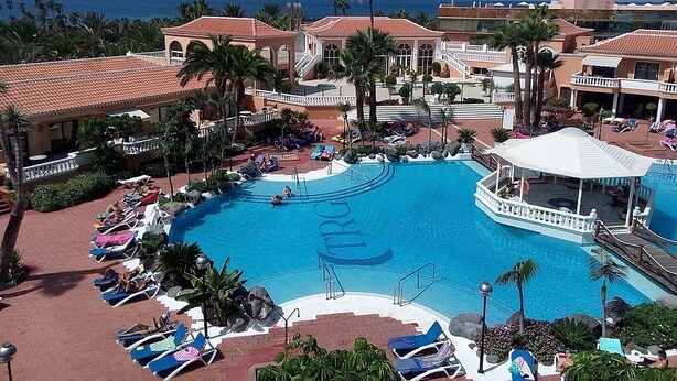 Een resort met een groot zwembad, palmbomen en uitzicht op de oceaan.