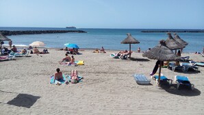 Een strand met ligbedden, parasols en rieten zonnedaken.