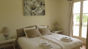 A neatly made double bed with two pillows, a bedside table with a lamp, and a painting of a flower on the wall.