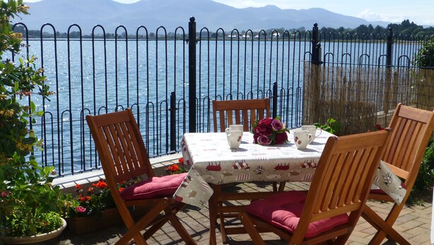 A table set outdoors with chairs, a view of a lake, and mountains in the background.