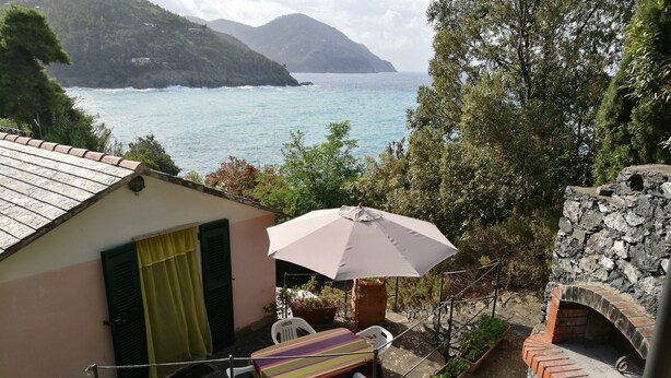 A terrace with a table and chairs, potted plants, and a view of the sea and mountains. - Seaside holiday home in Bonassola, Madonnina della Punta, near Cinque Terre (bonassola)