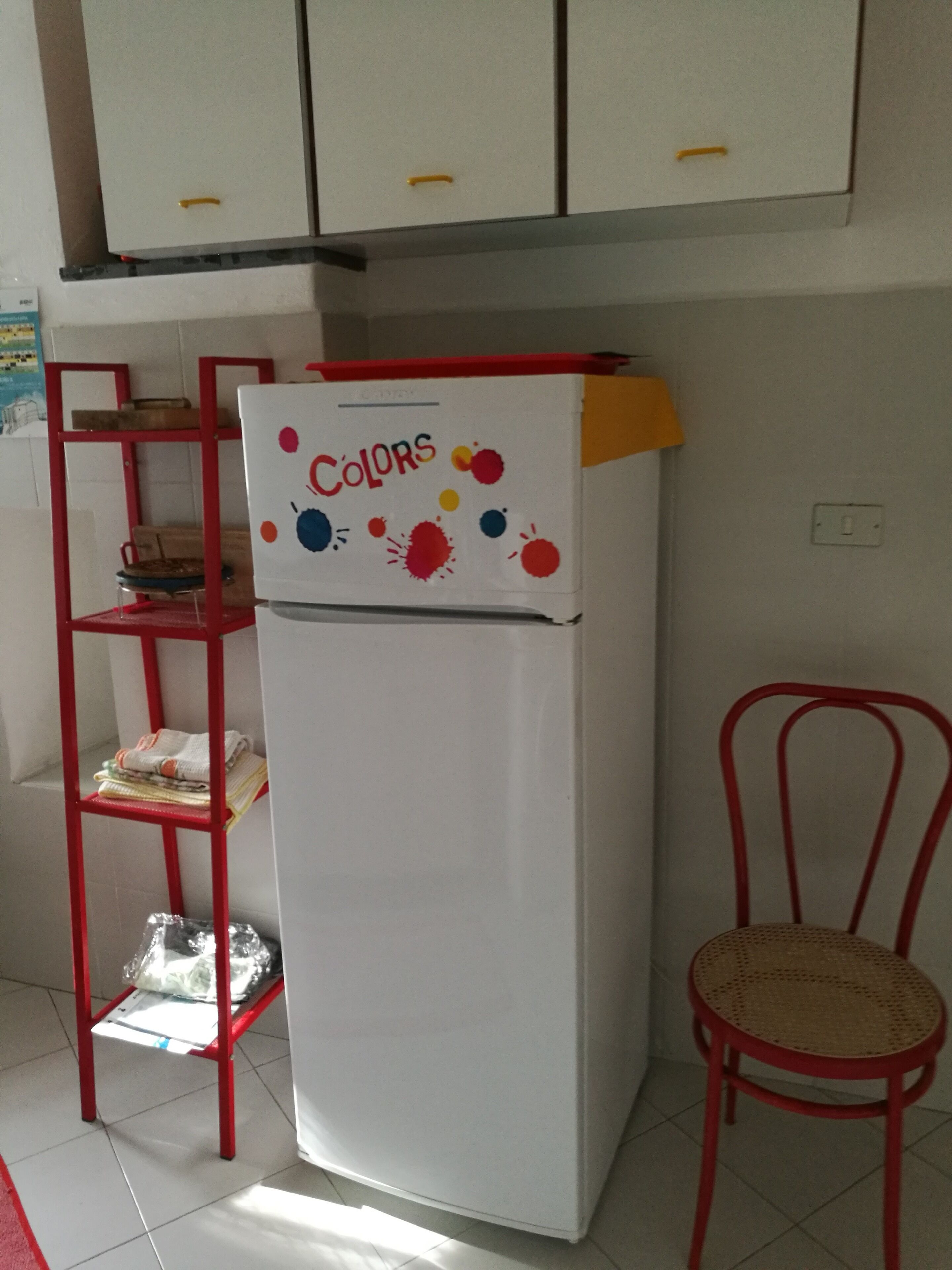Una cocina con un refrigerador blanco, una silla roja y una estantería metálica roja.